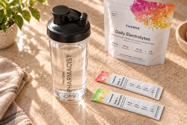 That One Pharmacist shaker filled with still water, viewed from above with Thorne electrolyte sticks on the counter and a softly blurred variety bag behind